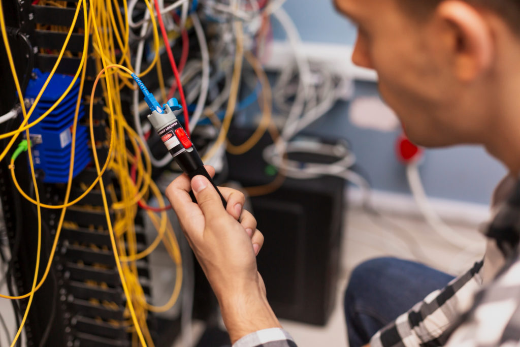 Technician using a visual fault locator to test single-mode fiber optic cables in a data center